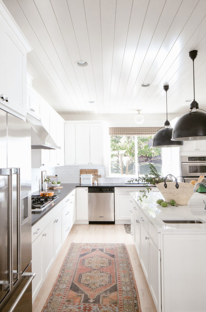 White kitchen with large black pendants, vintage rug and contrasting countertop