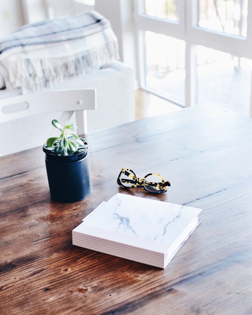 Book, glasses and plant on table in a light and airy room.